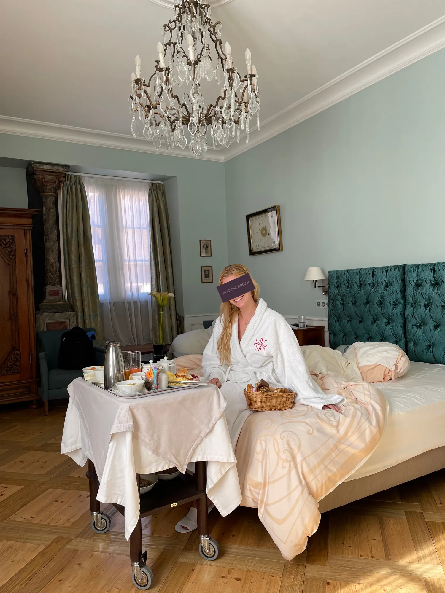 Adeline in a white bathrobe beside a breakfast trolley in a hotel room