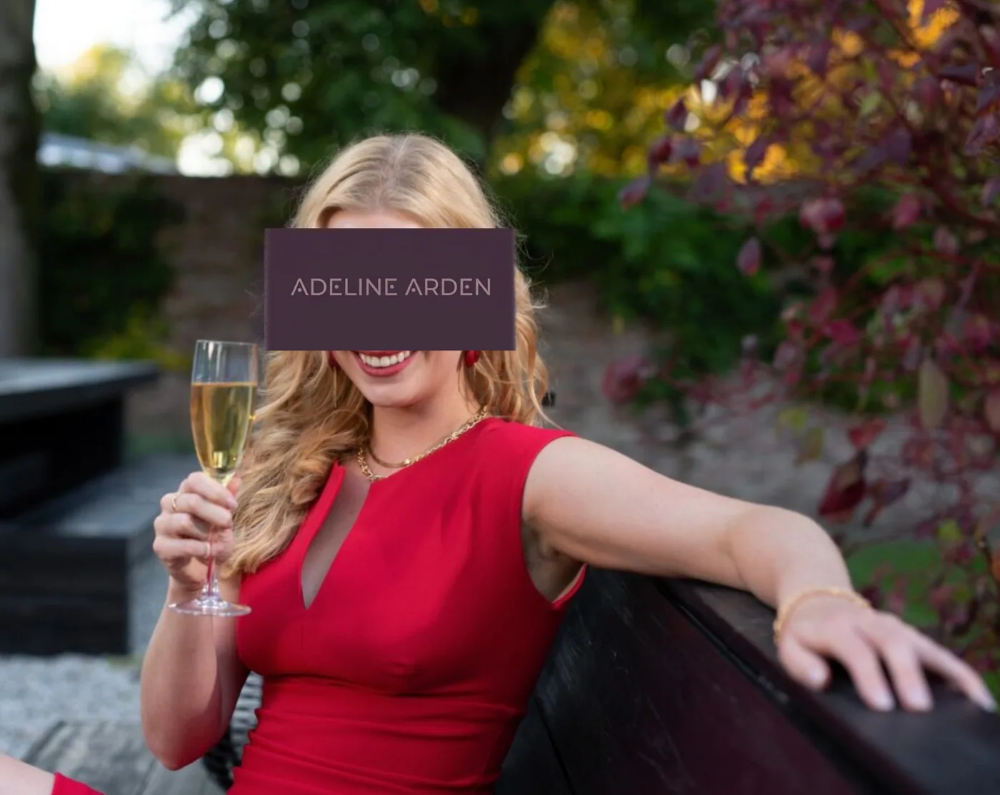 Adeline in an oxblood dress holding a champagne glass