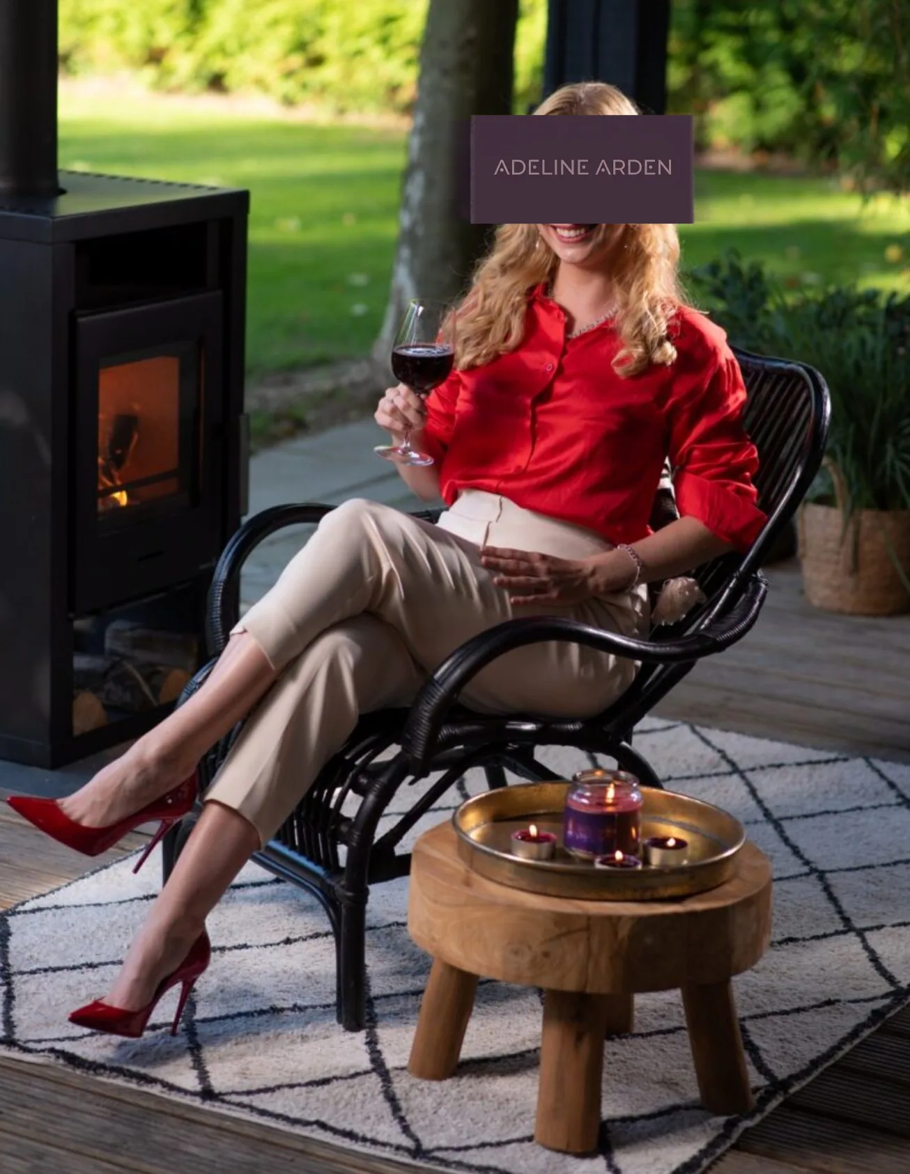Adeline dressed in red beside a fire with a glass of wine